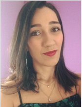 Aluna Adriana Guimarães Barrilao. Mulher jovem de pele branca, olhos castanhos, cabelo castanho pouco abaixo da altura dos ombros, Usa uma blusa de alças verde sobreposta por renda preta, dois colares dourados, sendo um com pingente redondo e outro com a letra A, brinco de argola e batom vermelho.