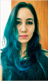 Aluna Fabrícia Heloísa Cavicchioli Sugiyama. Mulher jovem de pele branca, apresenta cabelos ondulados abaixo da altura do ombro de cor castanho escuro com partes azuladas devido à iluminação e olhos pretos. Está usando uma blusa preta com detalhes parecendo ramos em espirais de cor cinza-azulado e batom de cor rosa.