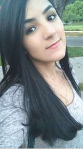 Aluna Katiane Tostes. Mulher jovem de pele branca, olhos pretos e cabelo preto de tamanho que ultrapassa os ombros. Ela está com a cabeça inclinada para a esquerda, blusa cinza de mangas, usa um colar dourado e tem semblante alegre.